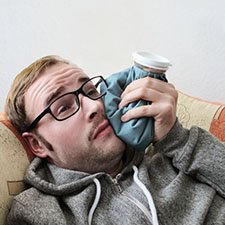man lying on a couch and holding a cold compress against his cheek 
