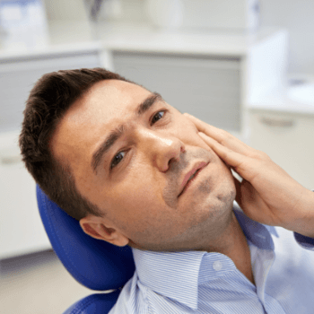 Man in need of emergency dentistry holding jaw in dental chair
