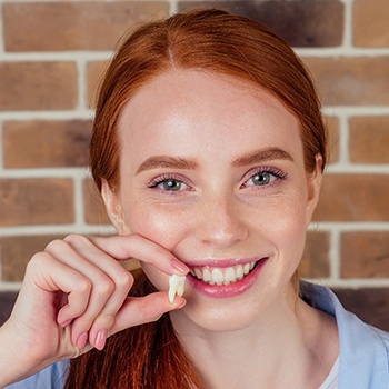 young woman smiling and holding up extracted tooth