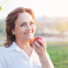 Senior woman with dental implants eating an apple
