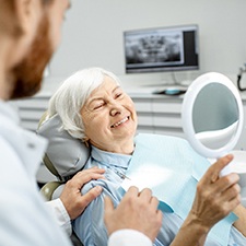 Woman with dental implant smiling in dentist's mirror