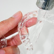 person rinsing their Invisalign aligner under running water 