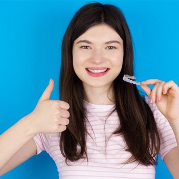 Teen girl holding clear aligner, making thumbs up gesture