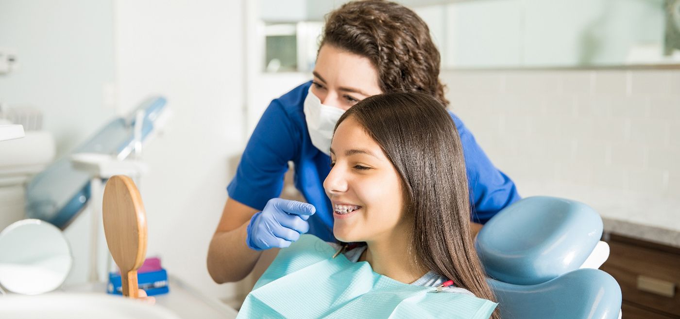 a dental hygienist pointing to a young girl with braces’ teeth