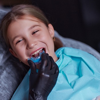 Dentist in black gloves inserting mouthguard into girl’s mouth