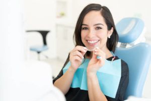 Woman in dentist’s chair holding clear aligner
